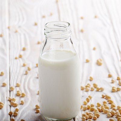 Non-dairy alternative Soy milk or yogurt in glass bottle on white wooden table with soybeans aside