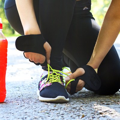A female athlete tying her shoe with a sports drink next to her