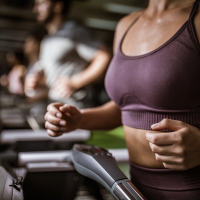 Unrecognizable athletic woman running on treadmill during sports training in a gym.