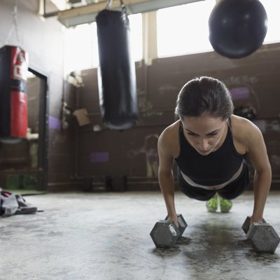 Strong female boxer doing push up exercise with dumbbells at gym
