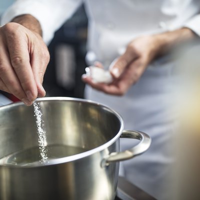 Chef putting types of salt in pan of water on stove, close-up