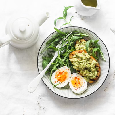 Healthy breakfast or snack - boiled egg, arugula salad and avocado toast on a light background, top view