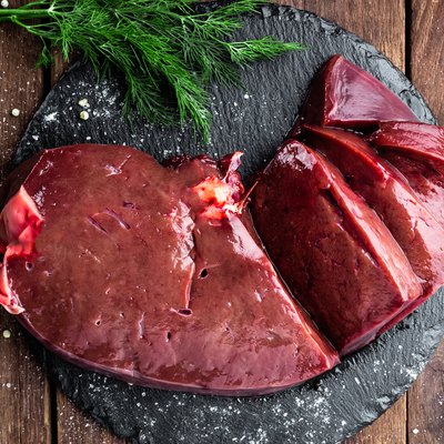 Raw liver on slate board on wooden background top view