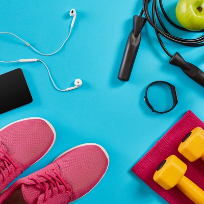 Flat lay shot of sneakers, jumping rope, dumbbells and smartphone on blue background