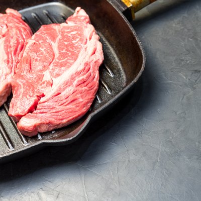 A raw marbled beef steak sits in a frying pan.