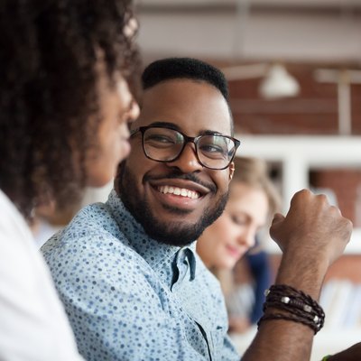 Smiling African American male employee look at colleague chatting