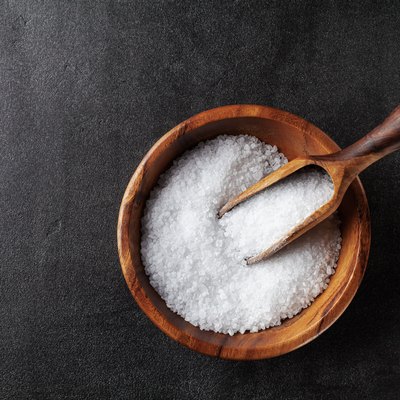 Salt in wooden bowl on black kitchen table top view.