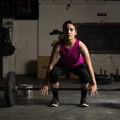 Young woman about to lift a barbell to perform deadlift variations