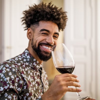 Smiling man drinking red wine during dinner party at home