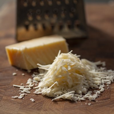 Grated italian parmesan cheese on wooden chopping board with a block of Parmesan and a grater in the background to bread proteins on a low-carb diet