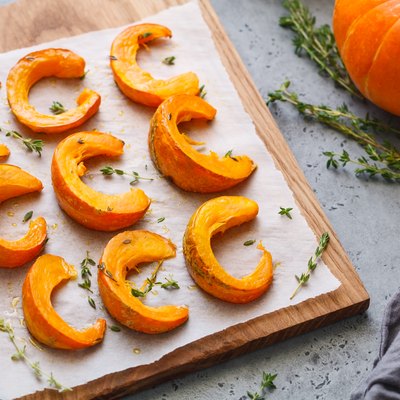 Baked pumpkin slices with thyme on a wooden board over grey table. Seasonal food vegetarian recipe.