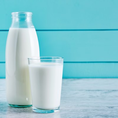 Bottle of milk and a glass full of milk on a wooden table against turquoise wooden background. Close up view.