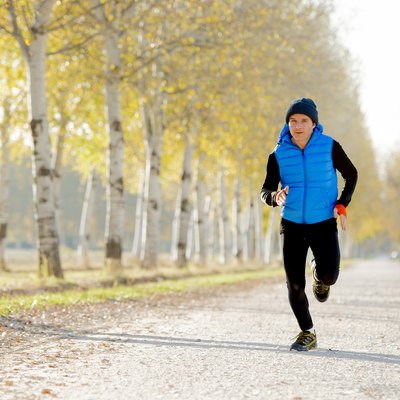 sport man running off road with trees under Autumn sunlight and wearing a running vest