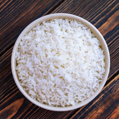 A Cup of white rice on a dark wooden background. Dietary or vegetarian food. Top view. Food cooked at home.