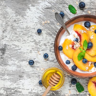 bowl of greek yogurt with peach, oats, nuts, mint, honey and blueberries with a spoon for healthy breakfast