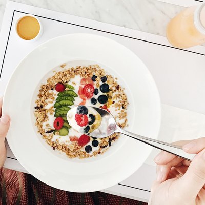 Healthy breakfast with plant based food like granola topped with natural yoghurt, kiwi, raspberry, blueberry, passion fruit served with honey