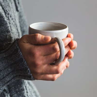 Woman in woolly gray sweater holding warm cup of tea