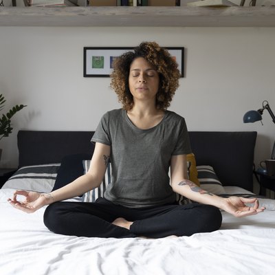 Woman practicing yoga, sitting on bed, meditating