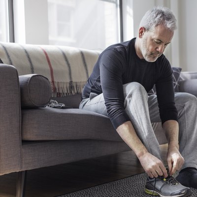 Full length of mature man wearing sports shoe at home