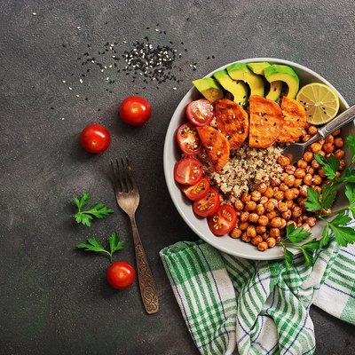 A bowl of healthy vegan and vegetarian lunch or dinner. Salad of fried chickpeas, quinoa, avocado, fried sweet potatoes and tomatoes on a dark painted background.Top view, flat lay