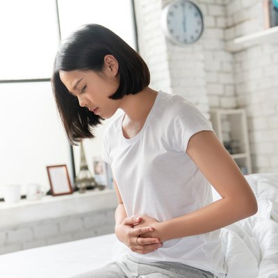 Asian women sitting in bed holding stomach with digestive problem