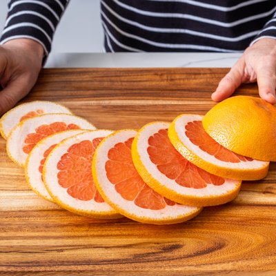 Caucasian woman hands placed on wooden chopping board with sliced red grapefruit and knife