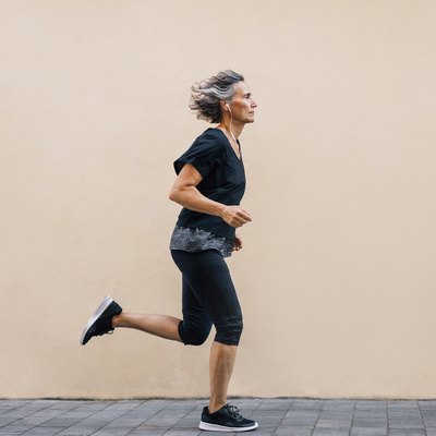 Side view of woman jogging on footpath against wall