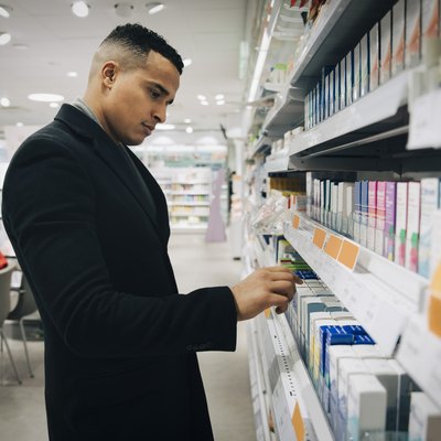 Side view of male customer choosing medicine from rack at pharmacy store