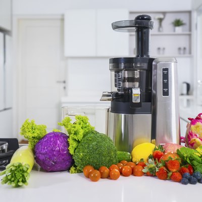 Juicer with various fruits and vegetables in kitchen