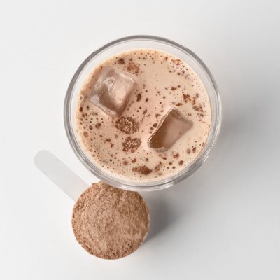 Glass with protein shake and powder in scoop on white background