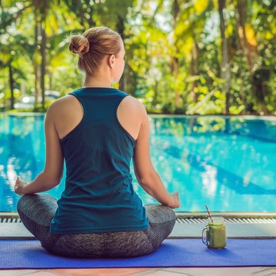 Closeup of a woman's hands during meditation with a green smoothies of spinach, orange and banana on the background of the pool