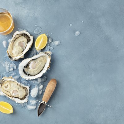Fresh raw oysters, shot from above on ice with a glass of white wine, lemon slices, shucking knife and copy space