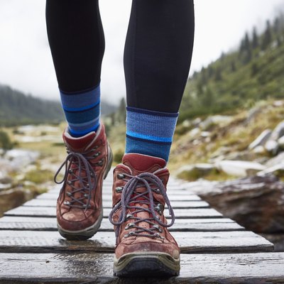 Female hiker hiking across wooden footbridge, cropped view of legs and hiking boots