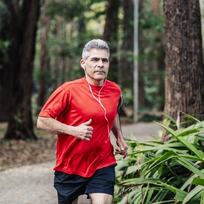 Mature man jogging in woods with earphones