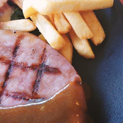 ham steak in white plate on wood table close up image.