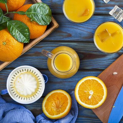 Orange juice in a glass, whole oranges, and sliced oranges on a blue wooden table.