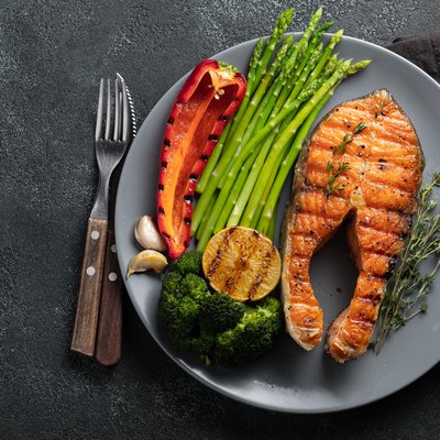 Tasty and healthy salmon steak with asparagus, broccoli and red pepper on a gray plate. Diet food on a dark background with copy space. Top view. Flat lay