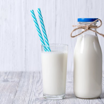 Bottle and glass of milk with straws, wooden background