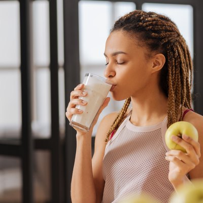 Young woman drinking glass of milk with apple in hand