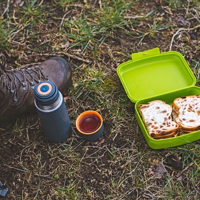 Shoe of hiker with thermos and lunch box in grass. Top view.