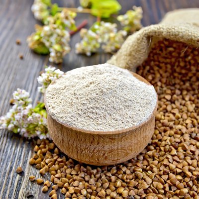 Flour buckwheat in bowl with cereals and flower on board