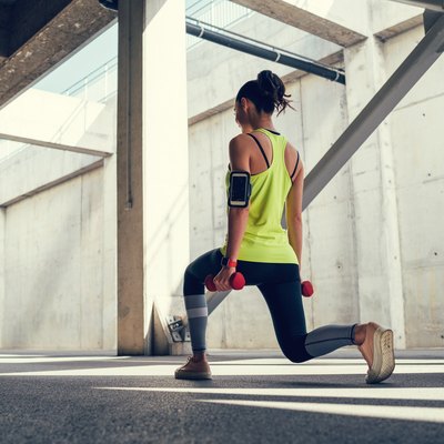 woman doing lunges with dumbbells outside for benefits of full-body workout