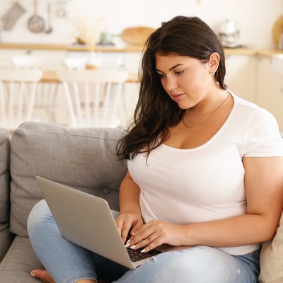 A woman sitting on the couch with her laptop to access a weight-loss forum
