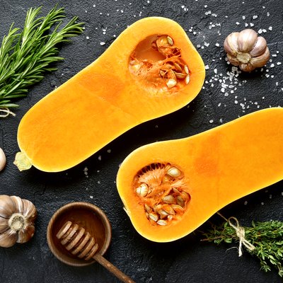 Halves of raw organic butternut squash with spices and ingredients for making