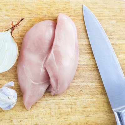 Top View of Raw Chicken Breasts, Fillets on a Wooden Cutting Board with Ingredients, Chopped Half Onion, Whole Garlic Bulb, and Stainless Chef Knife. Organic Food, Poultry Meat Cooking Concept