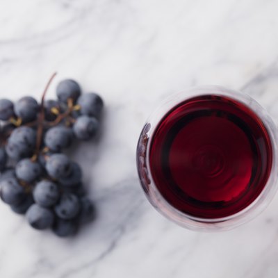 Red wine in glass with fresh grape on marble table background. Top view.