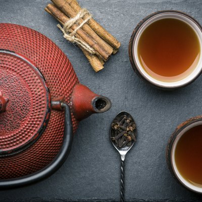 Tea composition with ceramic tea cups and red iron teapot on dark stone background