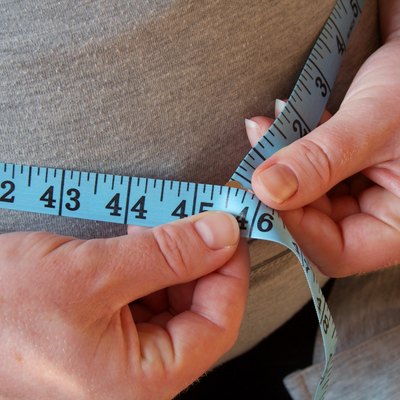 Close view of a woman using a measuring tape to measure her belly fat