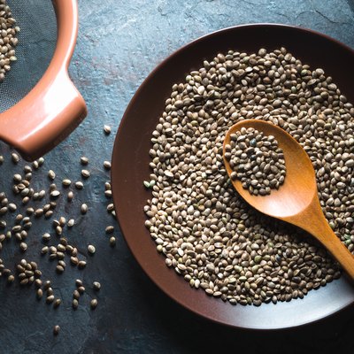 Hemp seeds on a plate and in a sieve on a gray blue stone
