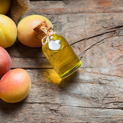 Glass bottle of Apricot seed kernel oil ( prunus armeniaca oleum ) with fresh ripe apricot fruits on wooden rustic background
